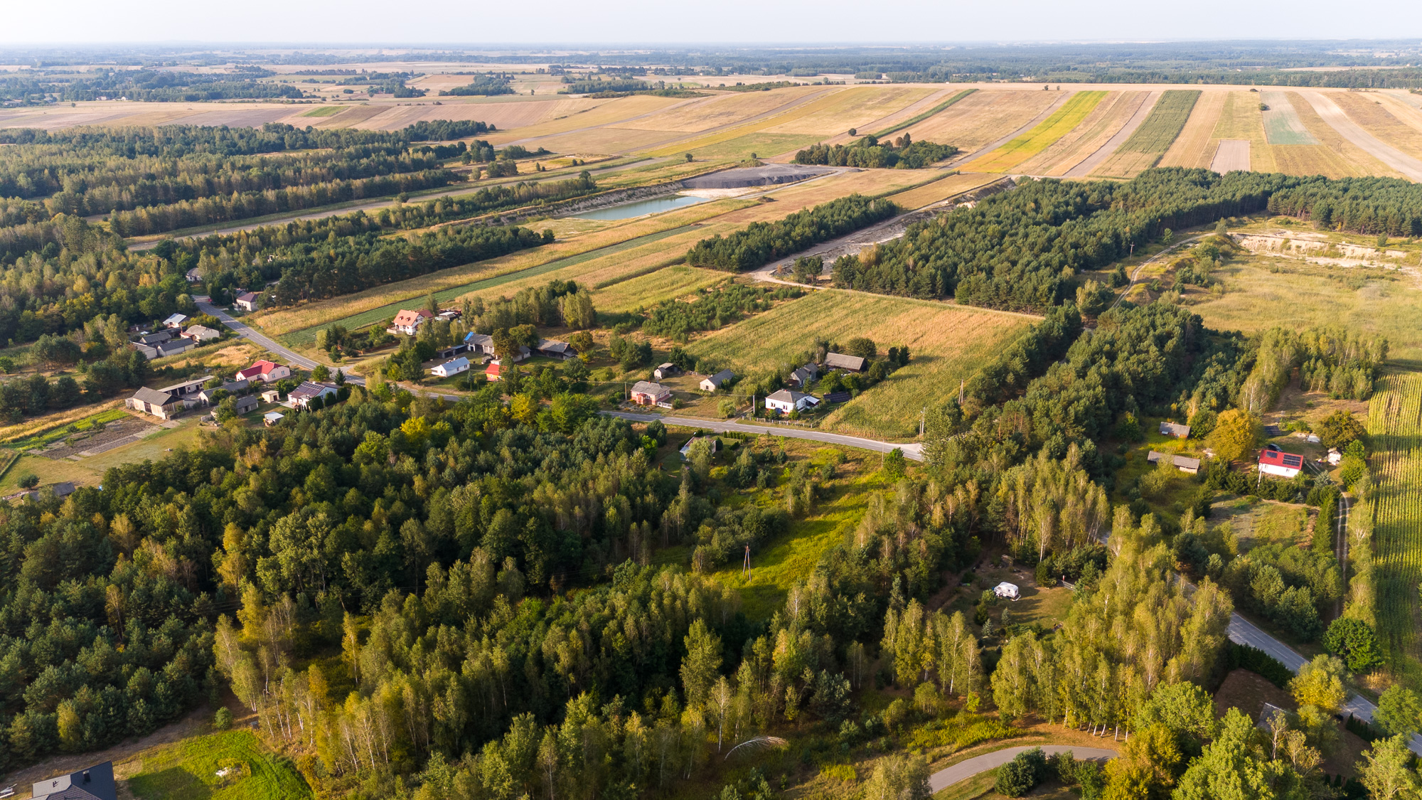 Widok z lotu ptaka na miejscowość Toruń - na zdjęciu las, droga, zabudowania i pola